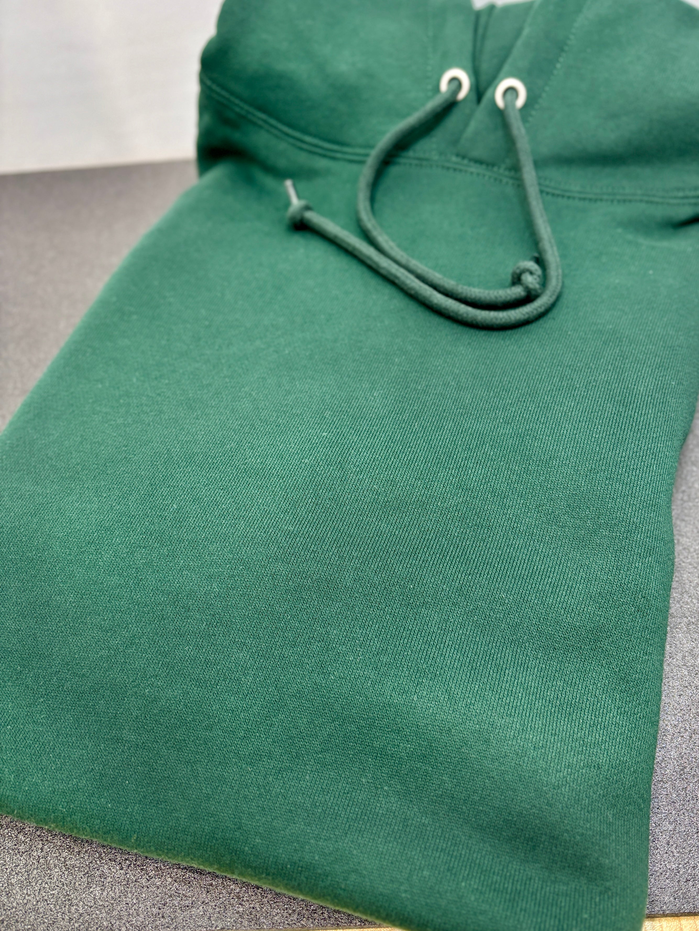 Green hoodie with a focus on the hood and drawstrings on a gray surface.