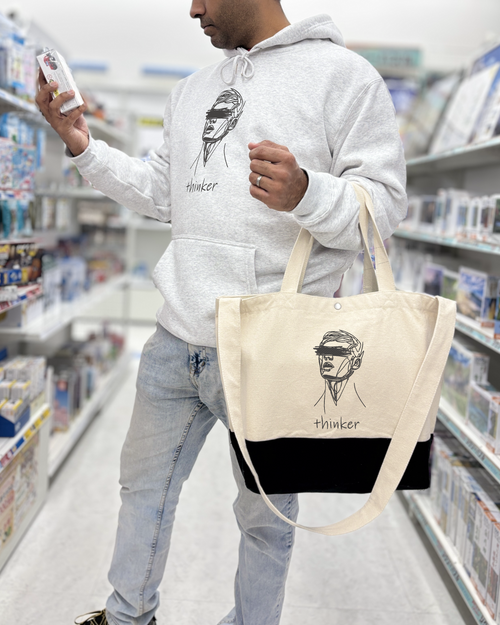 Man in a book familiafabrica.com holding a tote bag with a graphic design saying overthinker, looking at a book.